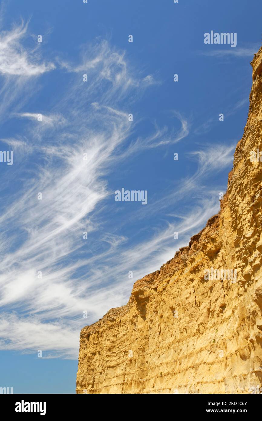 Stues Schwanzzirruswolken, die aus Eiskristallen gebildet wurden, über geschichteten Sandsteinklippen, Burton Bradstock, Dorset, Großbritannien, Juli. Stockfoto