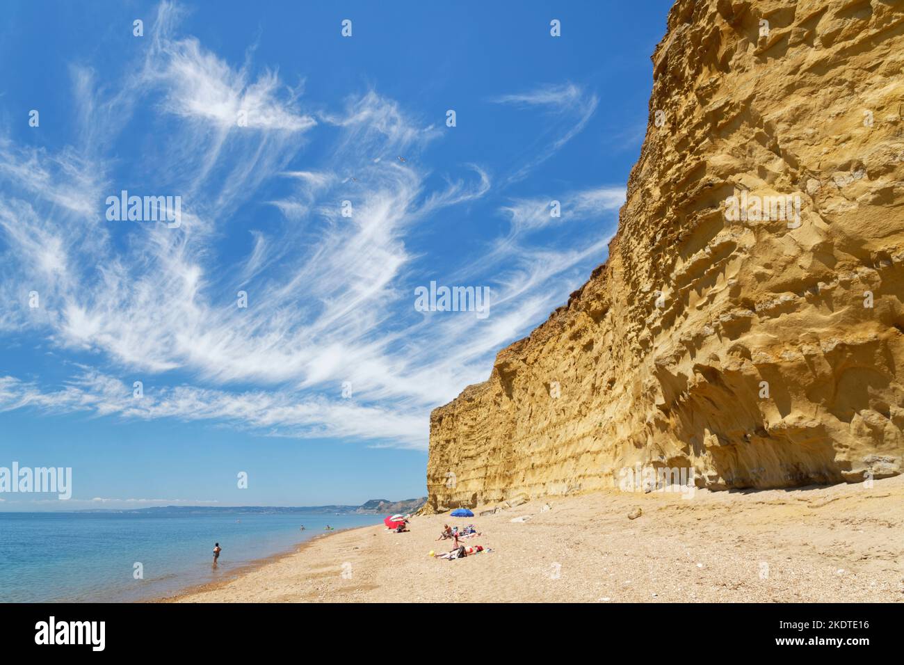 Menschen, die sich am Hive Beach entspannen, der von Sandsteinklippen mit Mare’s Schwanzzirrus-Wolken über dem Strand umgeben ist, Burton Bradstock, Dorset, Großbritannien, Juli. Stockfoto