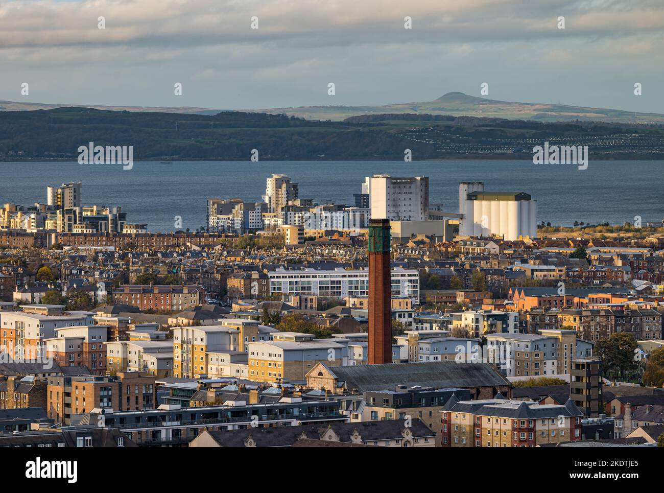 Blick über die Dächer auf den Firth of Forth mit einem industriellen Schornsteinturm und Hochhäusern. Edinburgh, Schottland, Großbritannien Stockfoto