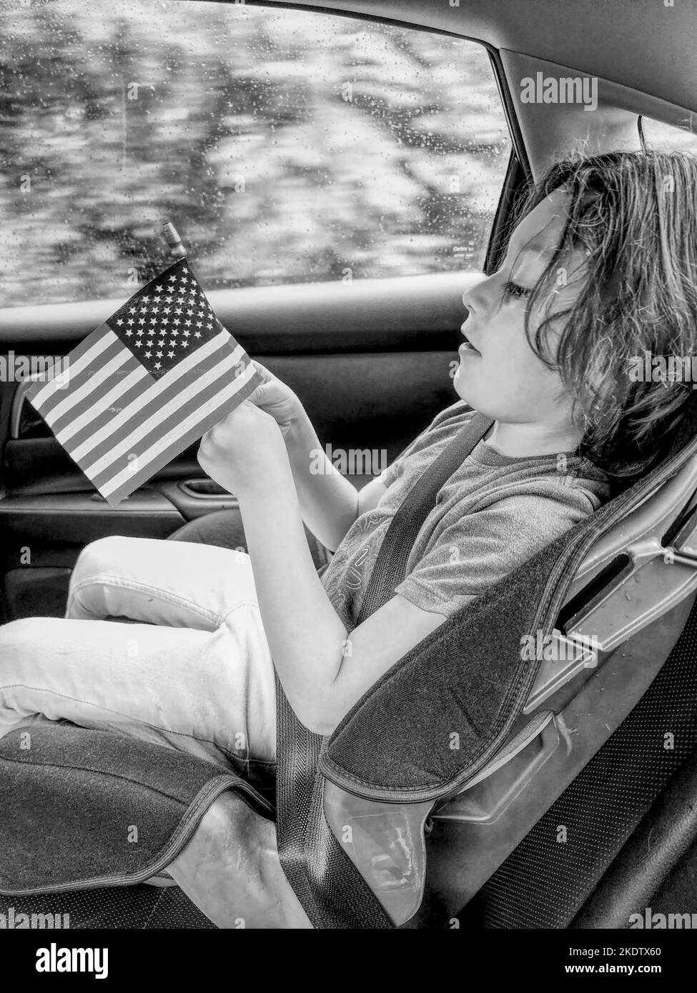 Ein kleiner Junge, der in einem Auto eine kleine amerikanische Flagge hält Stockfoto