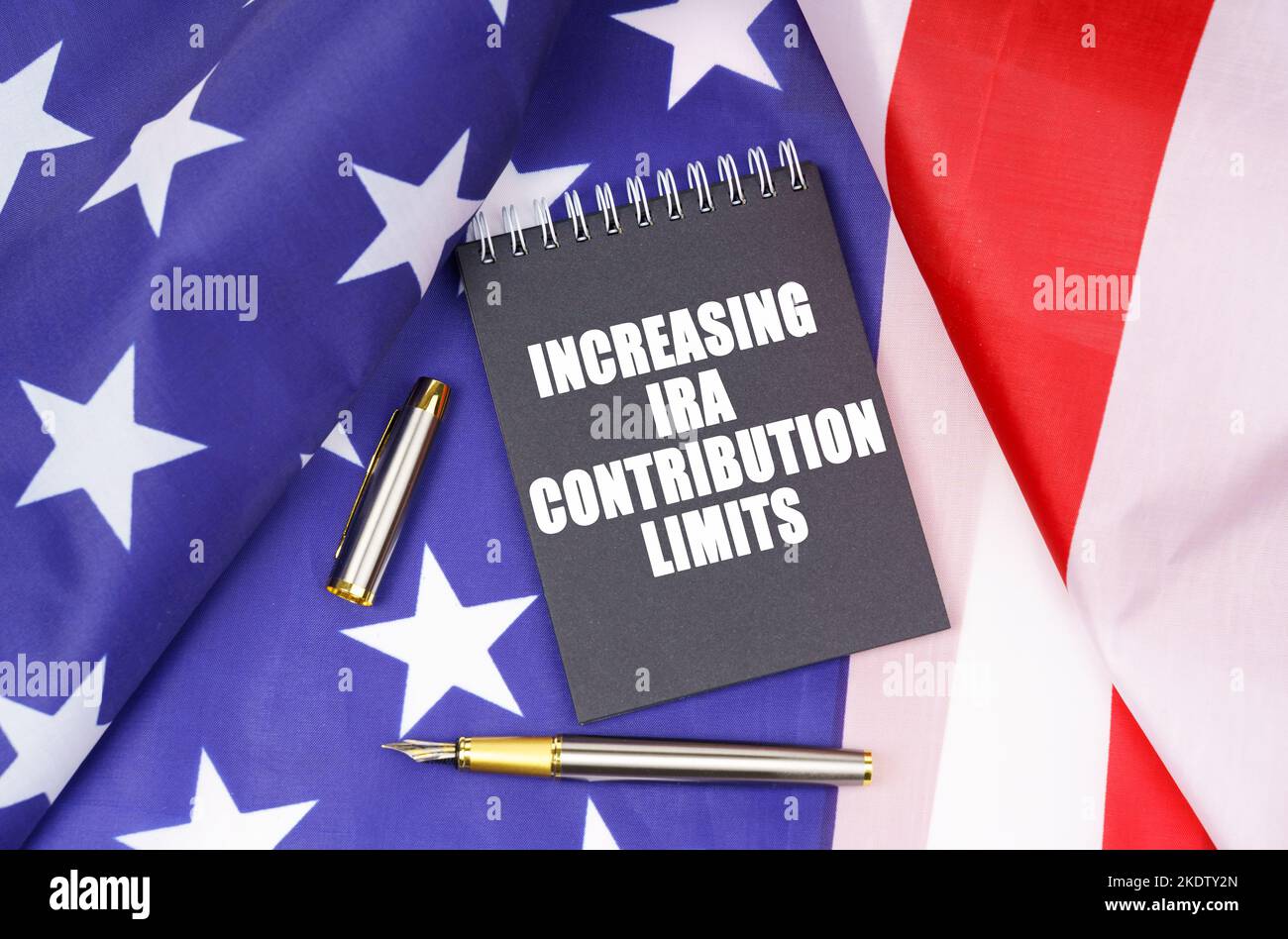 Geschäftskonzept. Auf der amerikanischen Flagge liegen ein Stift und ein Notizbuch mit der Aufschrift - Erhöhung der IRA-Beitragsgrenzen Stockfoto Geschäftskonzept. Auf der amerikanischen Flagge liegen ein Stift und ein Notizbuch mit der Aufschrift - Erhöhung der IRA-Beitragsgrenzen Stockfoto