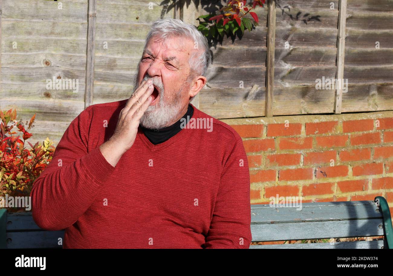 Älterer oder alter Mann mit der Hand zum Mund und Gähnen, weil er gelangweilt oder müde ist. Stockfoto