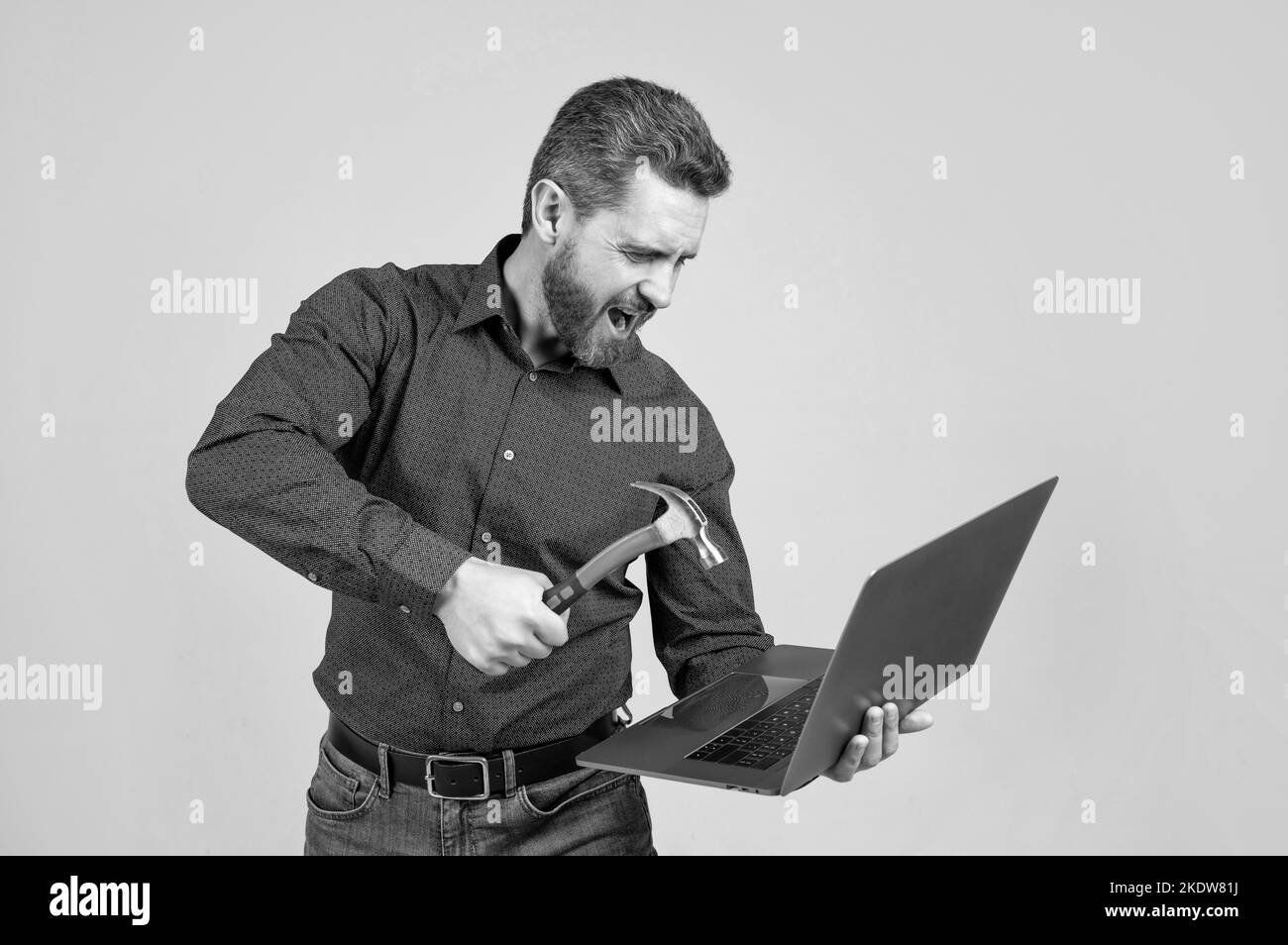 Wütender Mann schlug Laptop-Computer mit Hammer grauen Hintergrund, Absturz Stockfoto