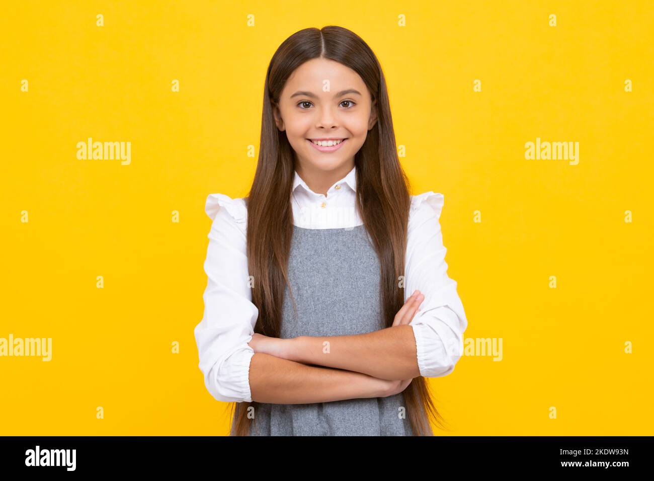 Glückliches Mädchengesicht, positive und lächelnde Emotionen. Selbstbewusstes Kind: Arme gekreuzt halten, isoliert auf gelbem Hintergrund, leerer Raum. Kleiner Kaukasier Stockfoto