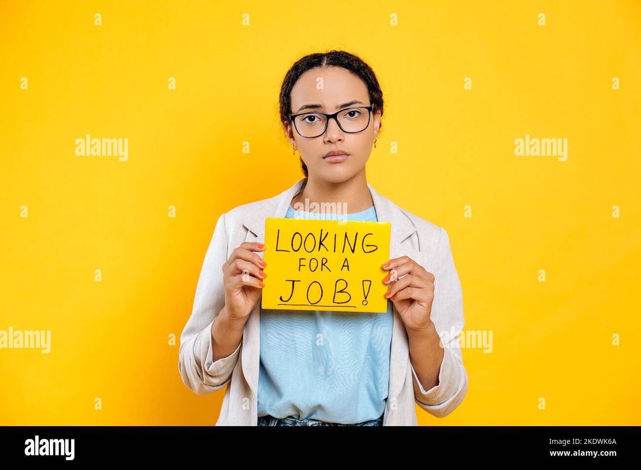 Frustriert traurig gemischte Rasse junge Frau mit Brille, kreative Spezialist auf der Suche nach einem Job, steht auf isoliertem orangefarbenen Hintergrund, zeigt ein Schild auf der Suche nach einem Job, schaut in Enttäuschung auf die Kamera Stockfoto