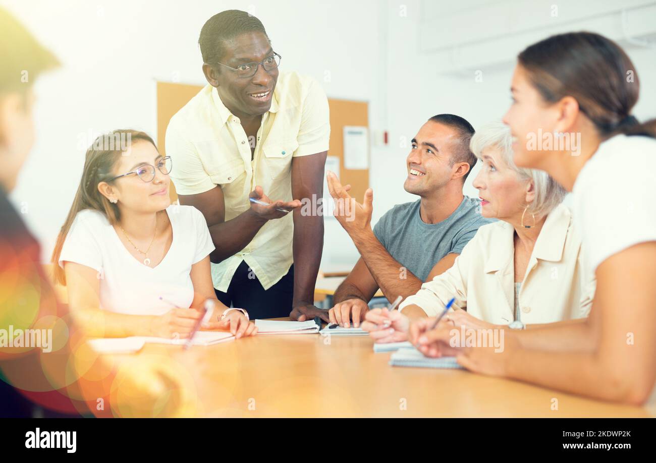 Freundliche afroamerikanische Englischlehrerin, die Sprachkurse für eine Gruppe von Erwachsenen gibt Stockfoto