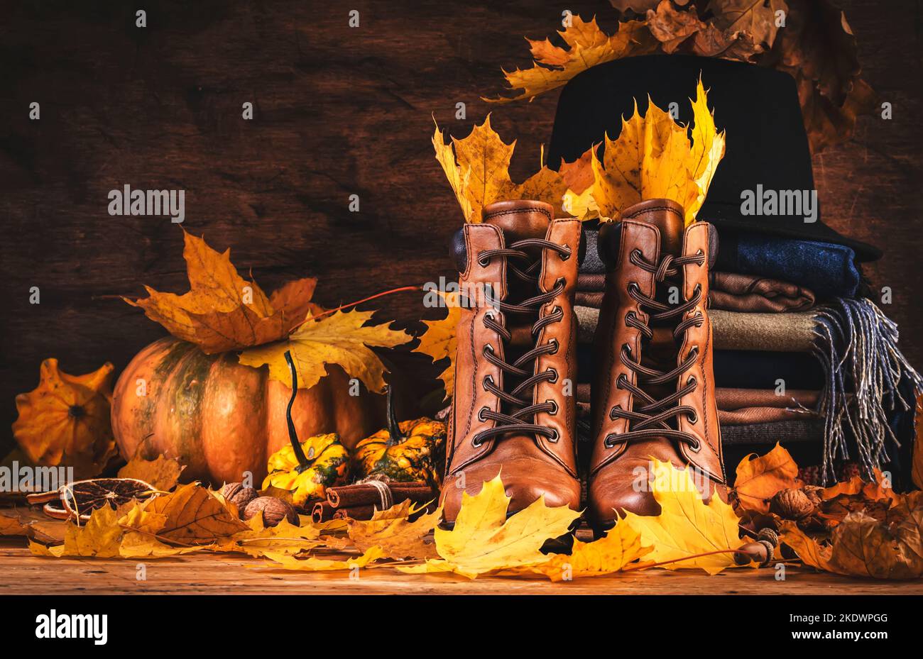 Herbsthintergrund mit braunen Lederstiefeln, herbstlicher warmer Kleidung, Halstüchern und Filzhut, Kürbissen, Ahorn- und Eichenblättern auf rustikalem Holzhintergrund. Land Stockfoto