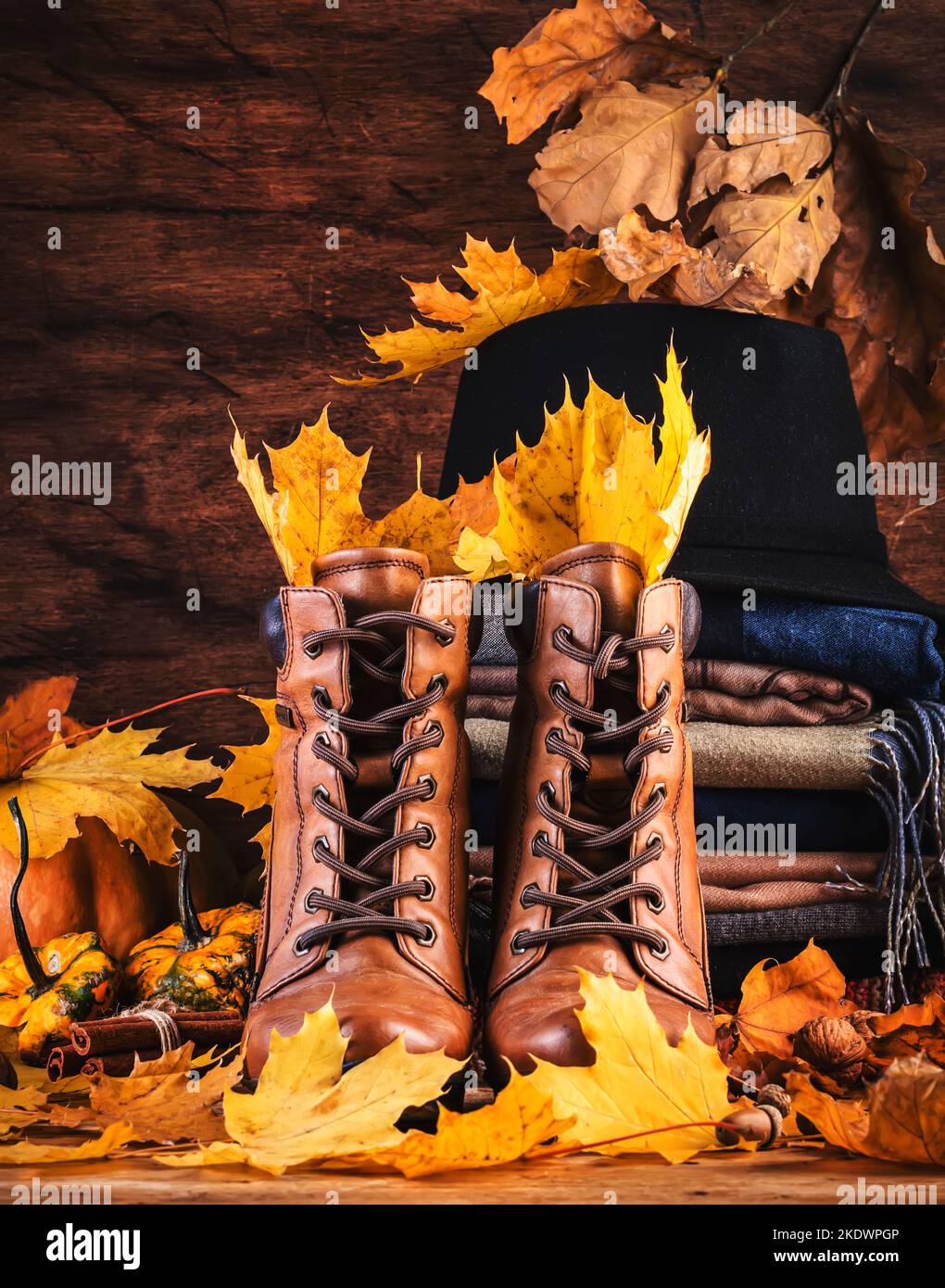 Herbsthintergrund mit braunen Lederstiefeln, herbstlicher warmer Kleidung, Halstüchern und Filzhut, Kürbissen, Ahorn- und Eichenblättern auf rustikalem Holzhintergrund. Land Stockfoto