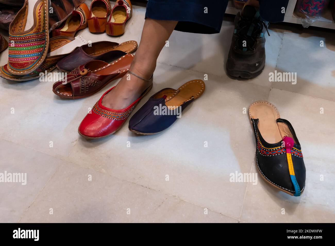 Schöne indische Frau, die ihren Fuß für das Anbringen von bunten Rajsathani Damenschuhen im Schuhgeschäft am berühmten Sardar Market und Ghanta Ghar Clock probiert Stockfoto