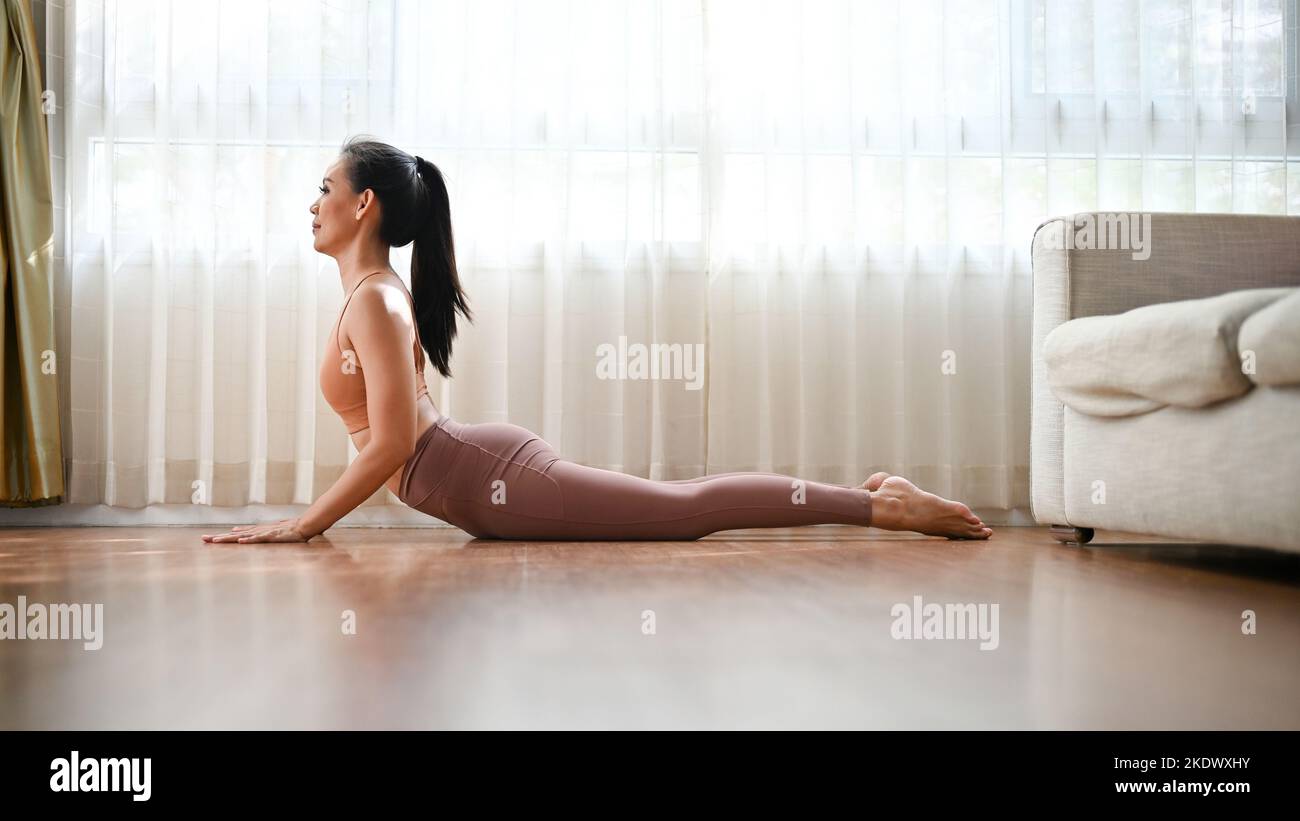Charmante asiatische Frau in Sportkleidung tut nach oben schauende Hund Yoga-Pose, Yoga üben ihr Wohnzimmer Stockfoto