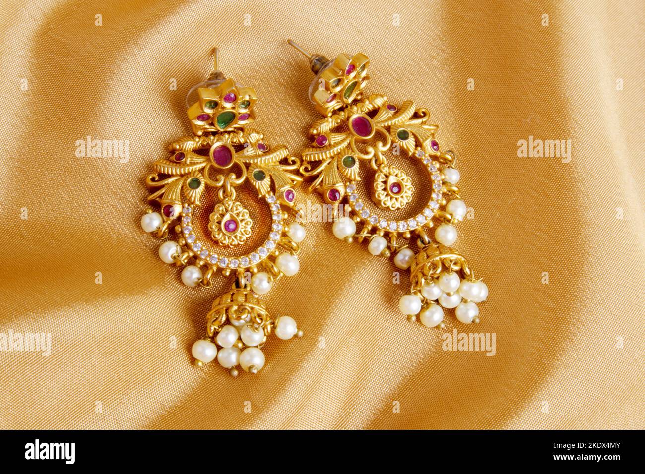 Ohrringe auf glatter, eleganter goldener Seide oder satinierter, luxuriöser Stoffstruktur als Hochzeitshintergrund. Luxuriöses Hintergrunddesign Stockfoto