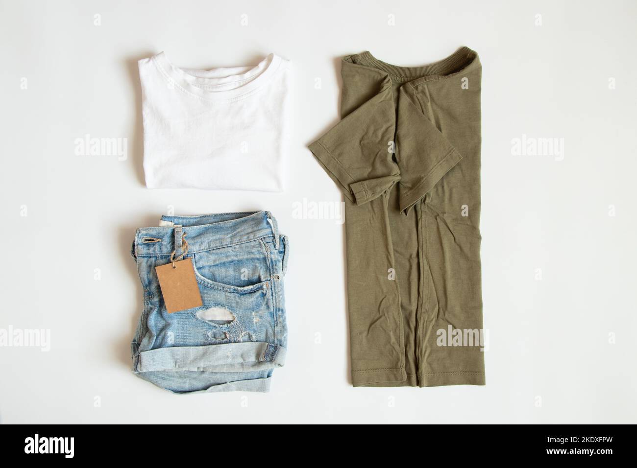 Weiße und grüne T-Shirts und Denim-Shorts liegen auf weißem Hintergrund mit einem Preisschild, einem Bekleidungsverkauf, einem Geschäft und einem Bekleidungsgeschäft Stockfoto