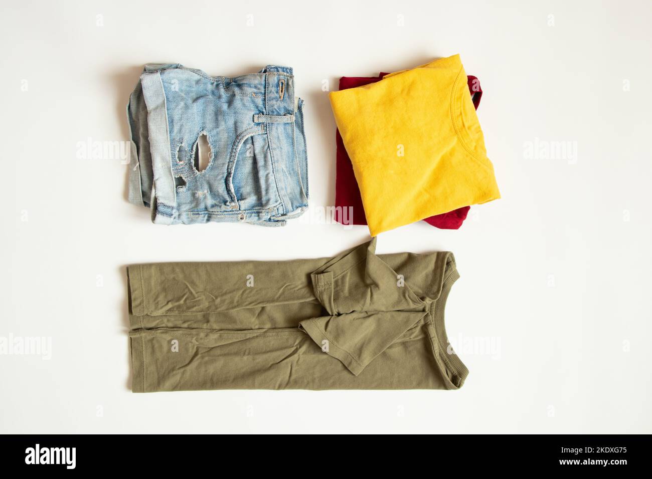 Rote, gelbe und grüne T-Shirts und kurze Denim-Shorts liegen auf weißem Hintergrund und legen Sommerkleidung auf weißem Hintergrund aus Stockfoto