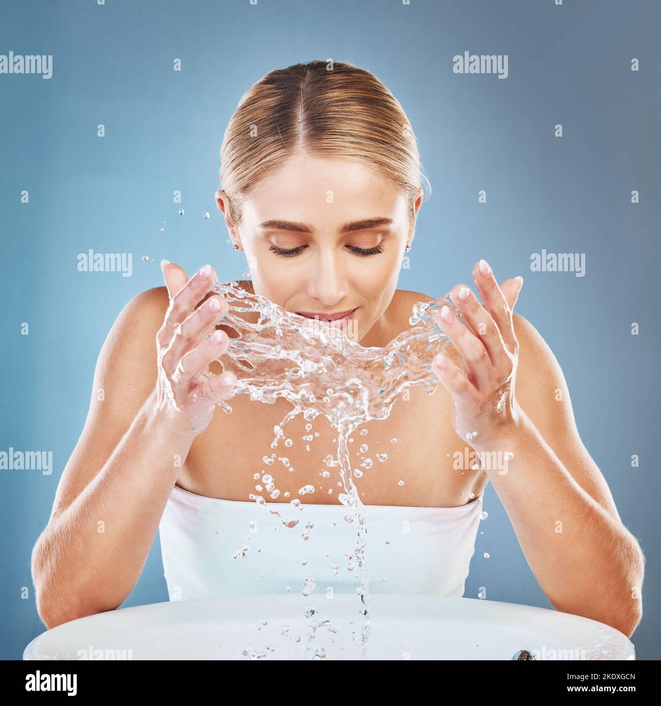 Gesicht, Wasser und Reinigung mit einer Model-Frau im Studio auf blauem Hintergrund, um ihre Haut im Waschbecken zu waschen. Spritzen, Hautpflege und Hände mit einem Stockfoto