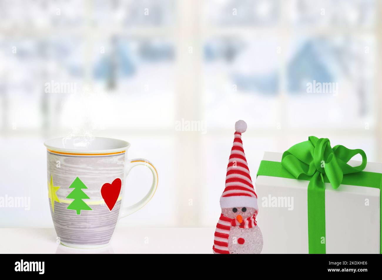 Frohe Weihnachten und Glückwünsche zum neuen Jahr. Ein Schneemann, ein Geschenkpaket und ein Weihnachtsbecher auf dem Tisch vor einer abstrakten Winterlandschaft. Sp Stockfoto