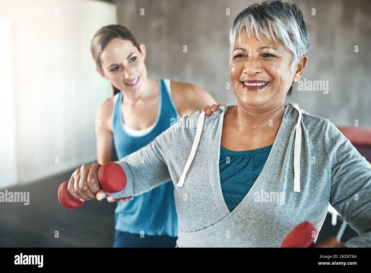 Fühlen Sie Ihr Bestes in jedem Alter mit regelmäßiger Bewegung. Eine ältere Frau mit Gewichten mit Hilfe eines Physiotherapeuten. Stockfoto