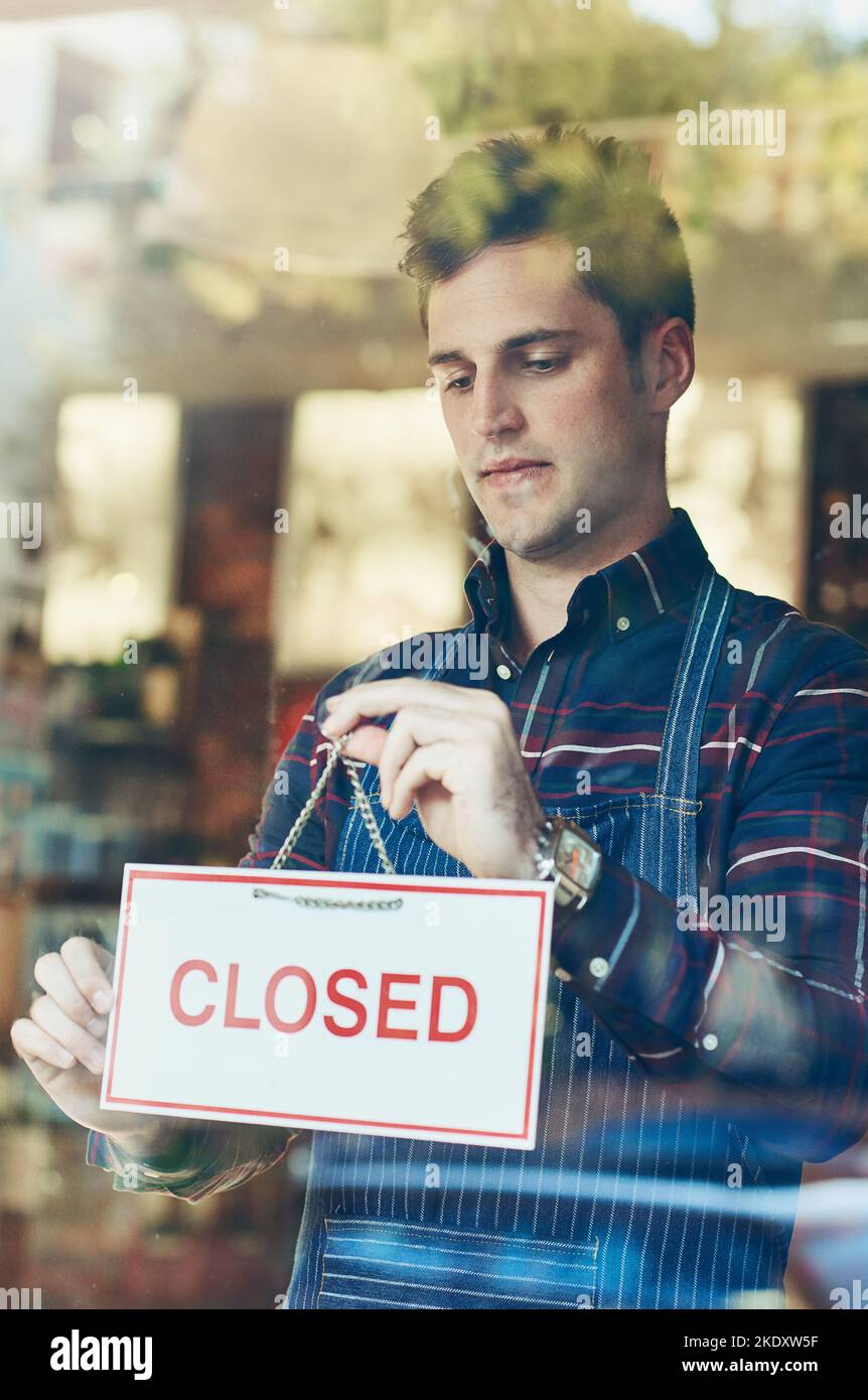 Zeit für Nahaufnahme für den Tag. Nahaufnahme eines jungen Mannes, der ein geschlossenes Schild an einem Schaufenster aufgehängt hat. Stockfoto