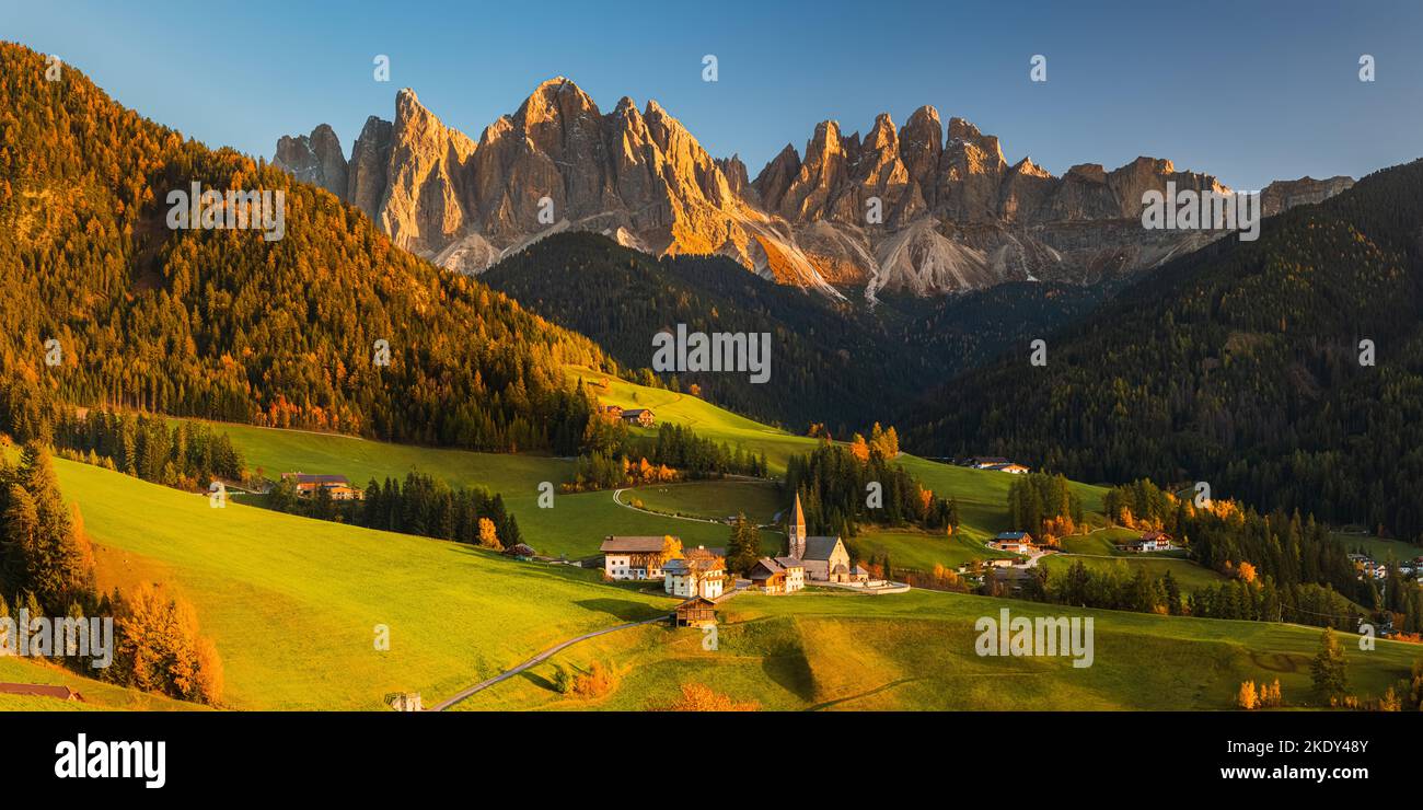 Ein Panoramabild aus dem Jahr 2:1 von einem herbstlichen Sonnenuntergang an der berühmten Kirche und dem Dorf Santa Maddalena vor dem Geisler- oder Geisler-Dolomiten-Gipfel Stockfoto