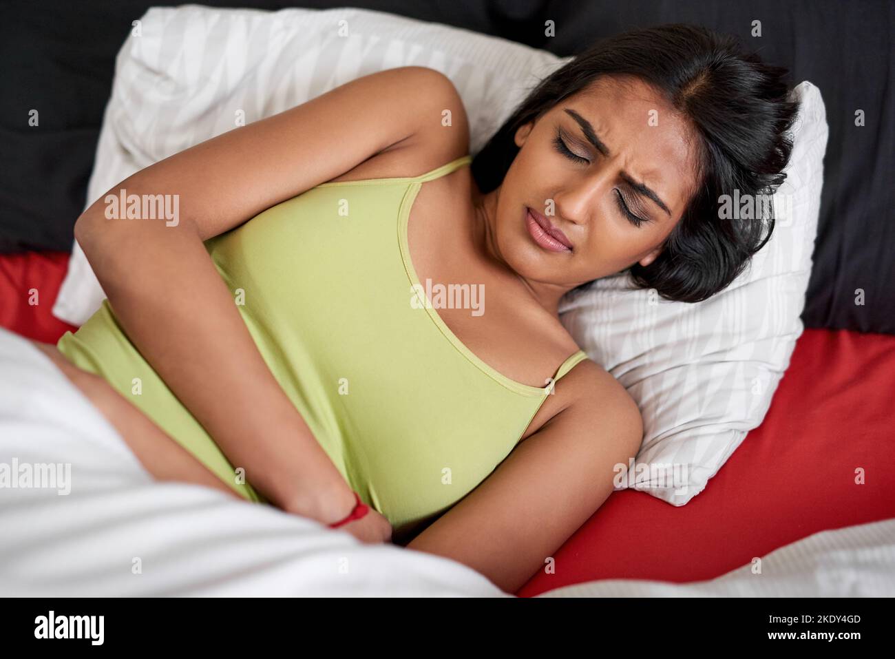 Eine junge Frau, die im Bett liegt und unter Bauchschmerzen leidet. Stockfoto