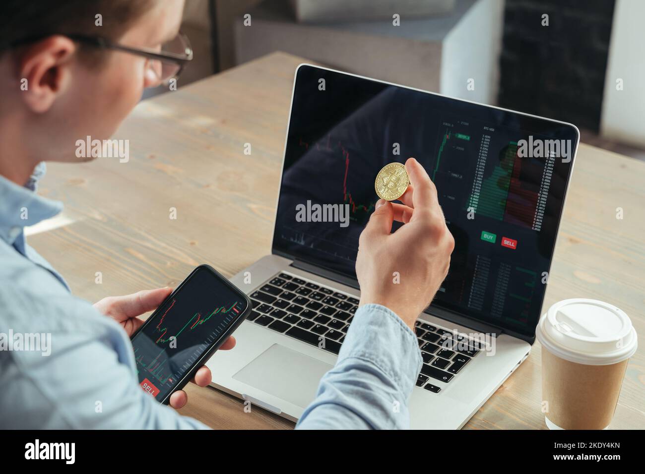 Nahaufnahme eines erfolgreichen Mann Krypto-Traders oder Brokers, der Gold Bitcoin hält, mit einem Laptop am Bürotisch sitzt, in BTC investiert und eine Kryptowährungs-App verwendet Stockfoto