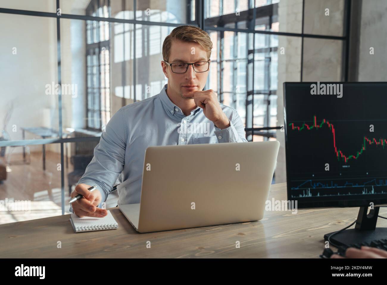 Männlicher Krypto-Trader, der an seinem Laptop im Co-Working Office arbeitet, mit konzentriertem und neugierigem Gesicht auf den Bildschirm schaut, sich ein Tutorial-Video über digitale Geldanlagen und Handelsstrategie ansieht Stockfoto