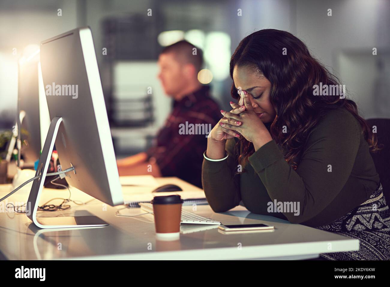 Eine müde und gestresste Geschäftsfrau, die an ihrem Computer arbeitet, während sie ihre Augen schließt und nachdenkt. Stockfoto
