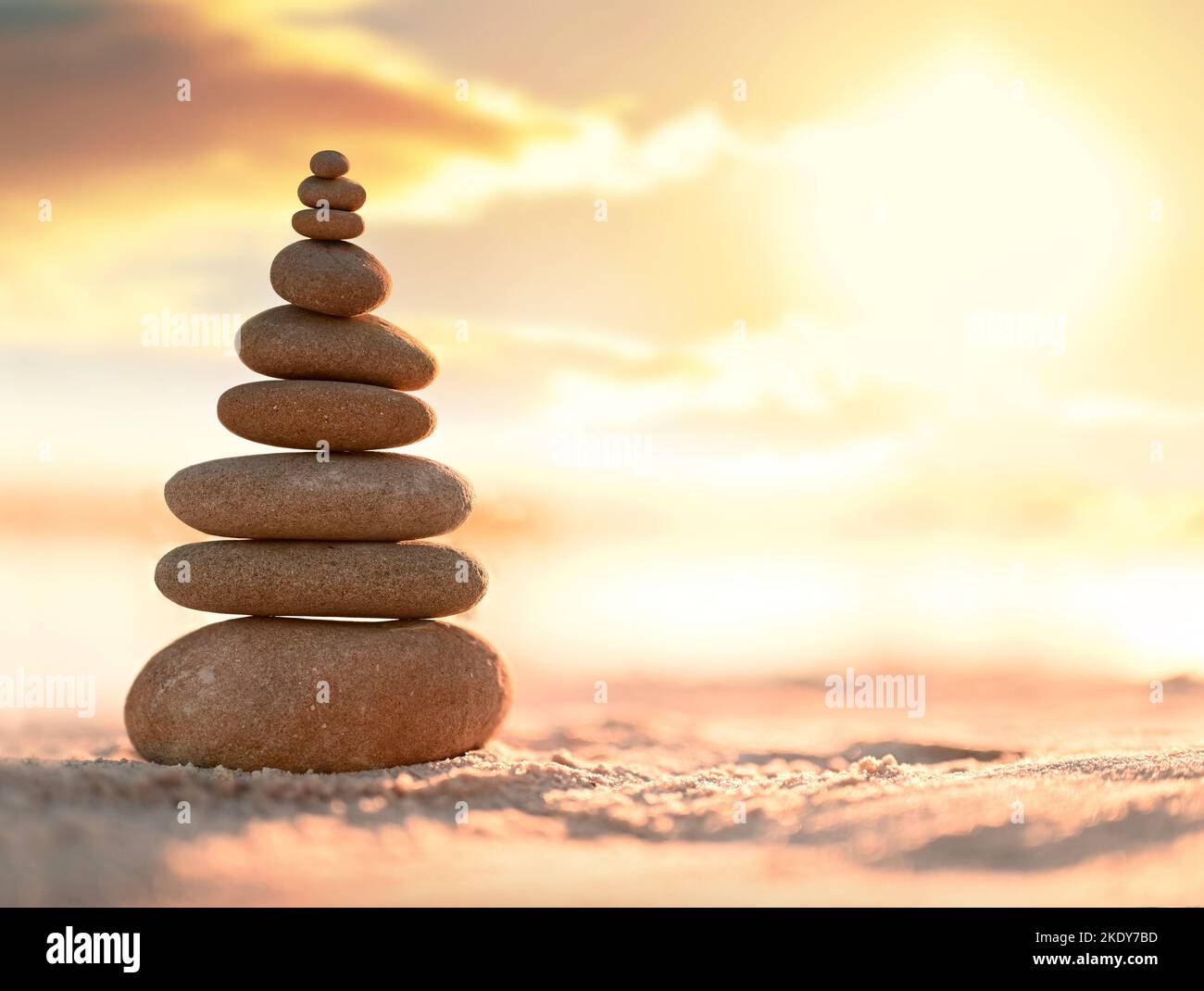 Ausgewogene Kieselsteinpyramide am Strand. Abstrakt warmer Sonnenuntergang Bokeh mit Sand auf dem Hintergrund. Zen-Steine am Meeresstrand, Balance-Konzept. Stockfoto