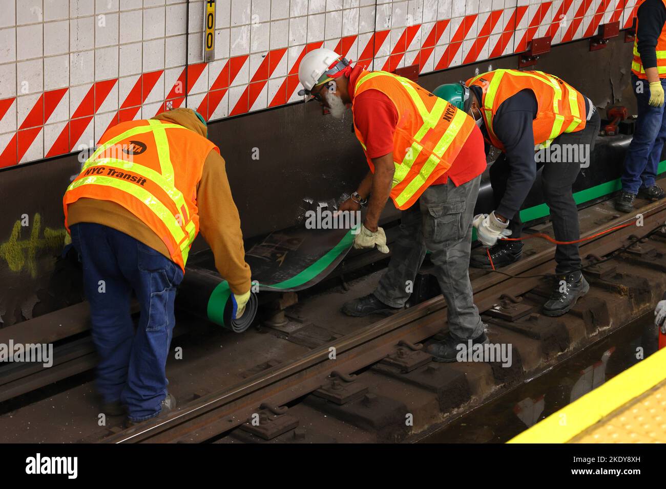 Mitarbeiter der U-Bahn-Gleise von NYC Transit legen eine schützende Gummiisolierdecke über die dritte Schiene als Teil sicherer Arbeitsverfahren und -Verfahren. Stockfoto