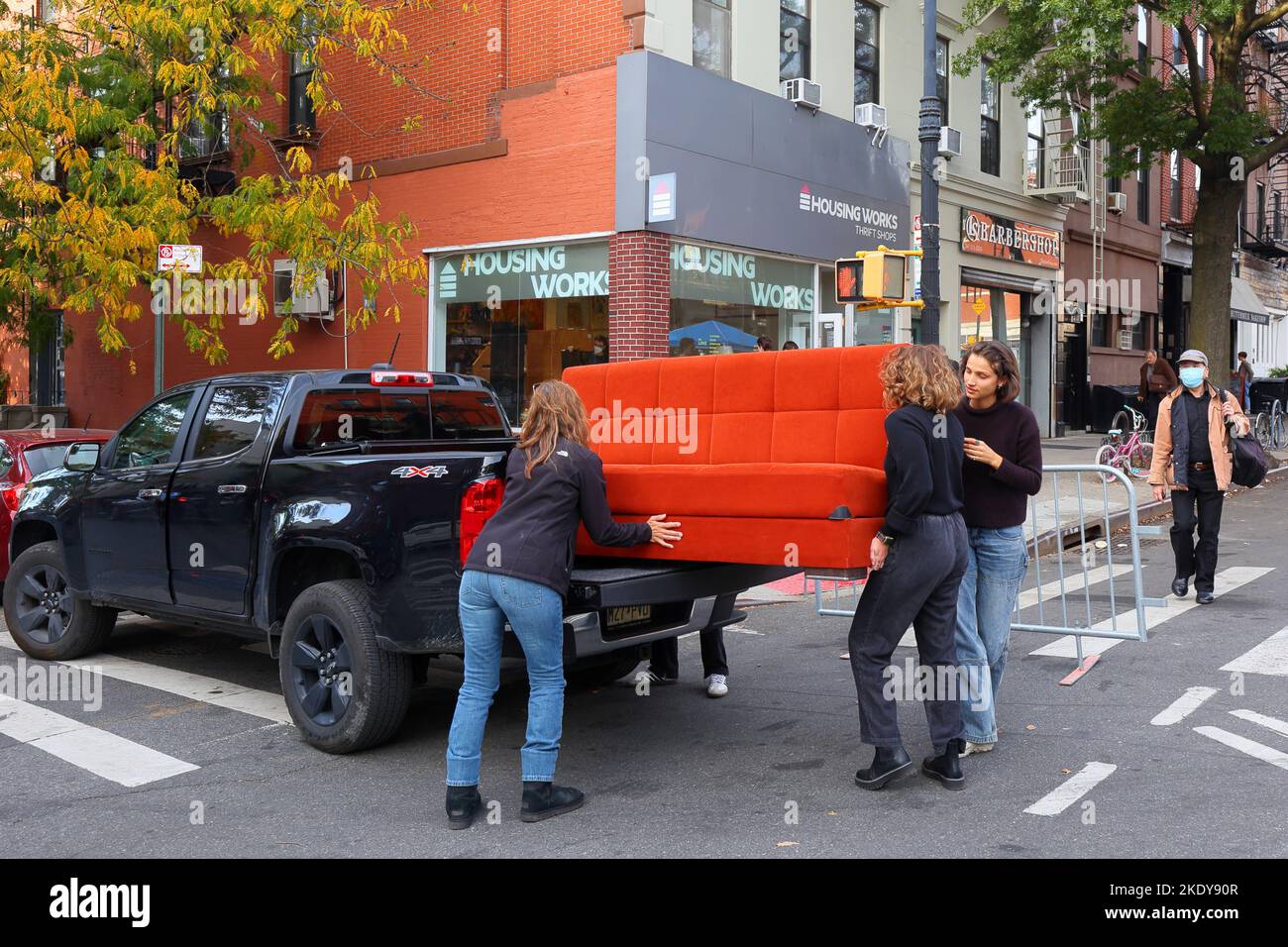 Drei Personen laden vor einer Housing Works in Brooklyn eine orangefarbene Couch auf einen Pickup-Truck Stockfoto