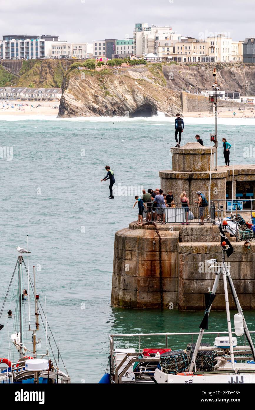 Ein junger Mensch in einem schwarzen Anzug springt vom Ende des Hafens von Newquay ins Meer. Stockfoto