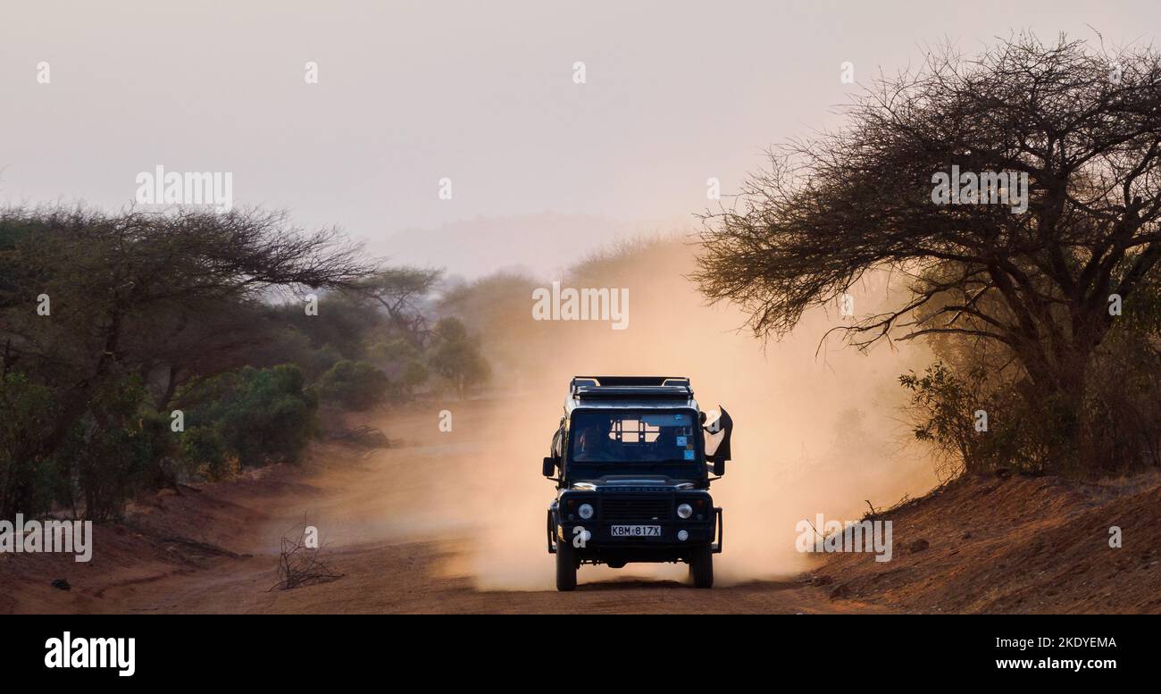 Land Rover Safari-Fahrzeug, das bei einer abendlichen Fahrt im Tsavo National Park in Kenia, Ostafrika, Staub aufwirbelt Stockfoto