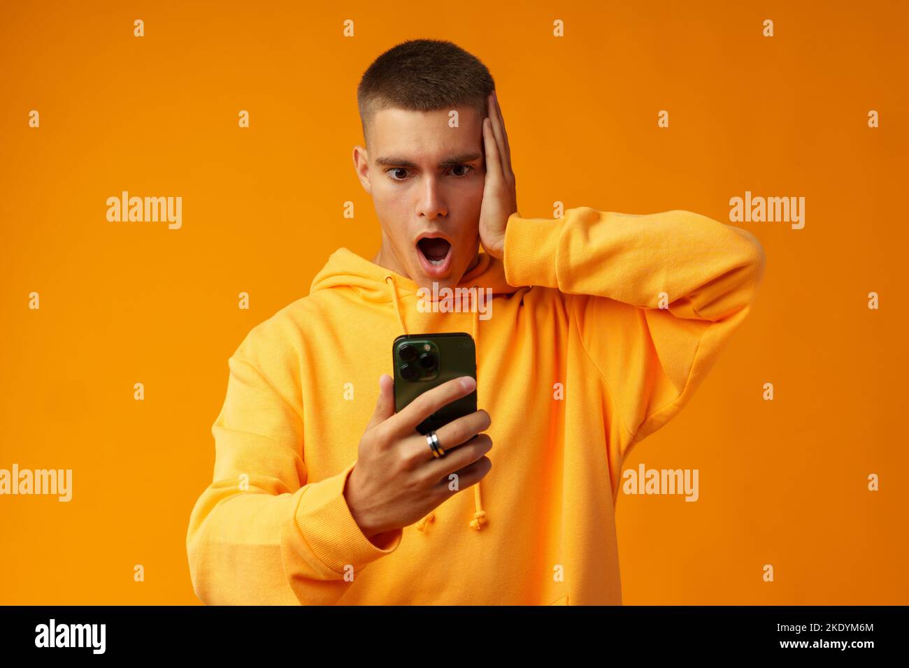 Junger Mann, der Negativität ausdrückt, während er die Nachricht auf dem Mobiltelefon auf gelbem Hintergrund liest Stockfoto