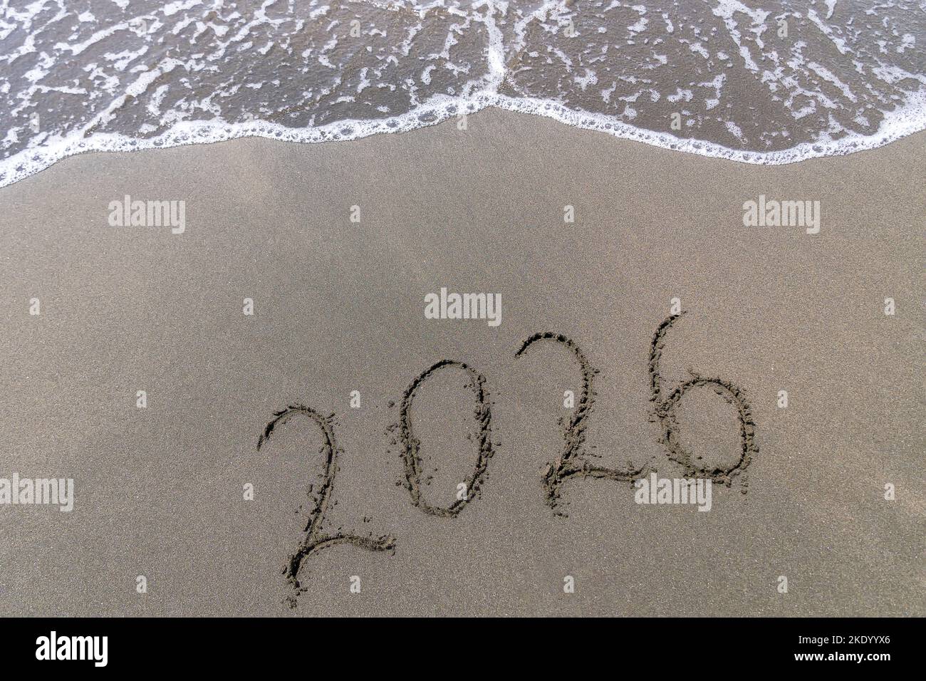Text Frohes Neues Jahr 2026 an einem Sandstrand mit kleiner Welle. Abstraktes Hintergrundbild des kommenden neuen Jahres 2023 Stockfoto