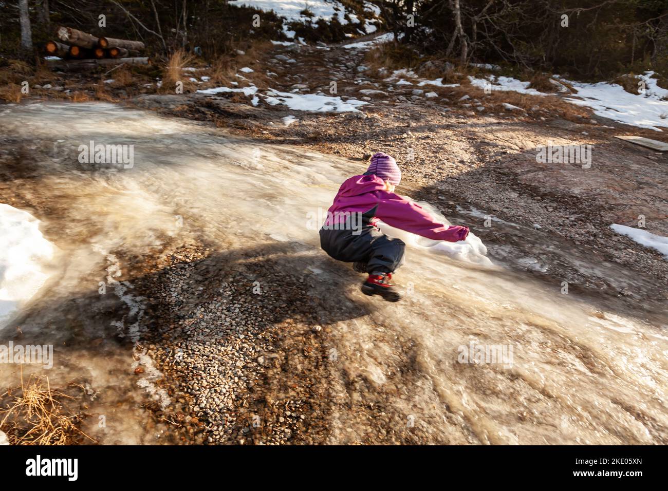 Ein junges Mädchen, das in einem Wald auf einem gefrorenen Bach rutscht Stockfoto