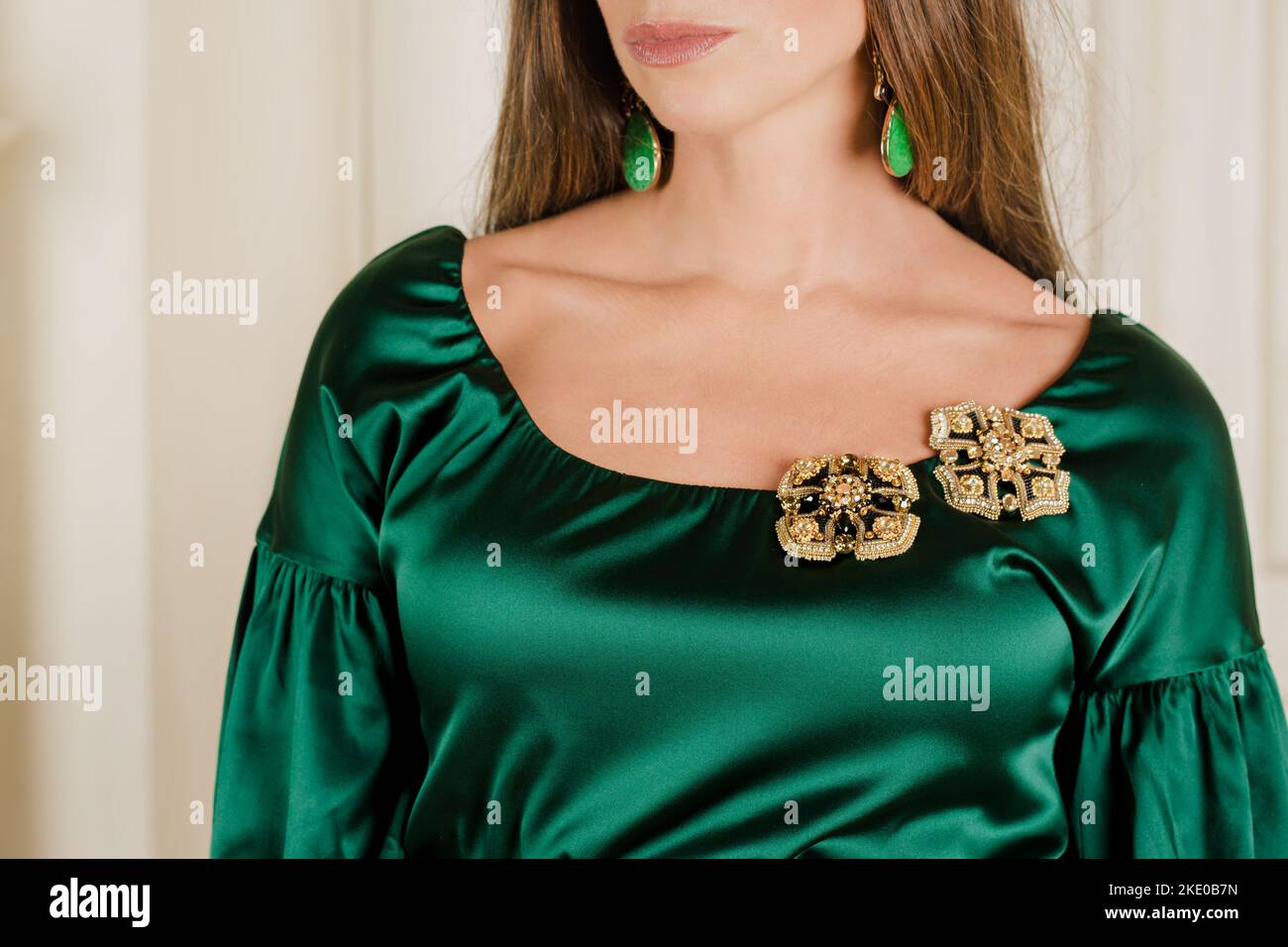 Eine schöne Frau in einem grünen Seidenkleid mit Broschen aus Perlen Stockfoto