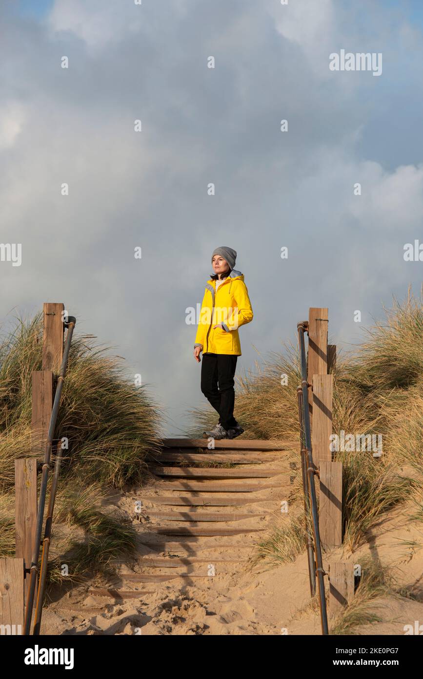 Frau mit gelbem Mantel, die auf den Sanddünen steht und die Aussicht betrachtet. Stockfoto