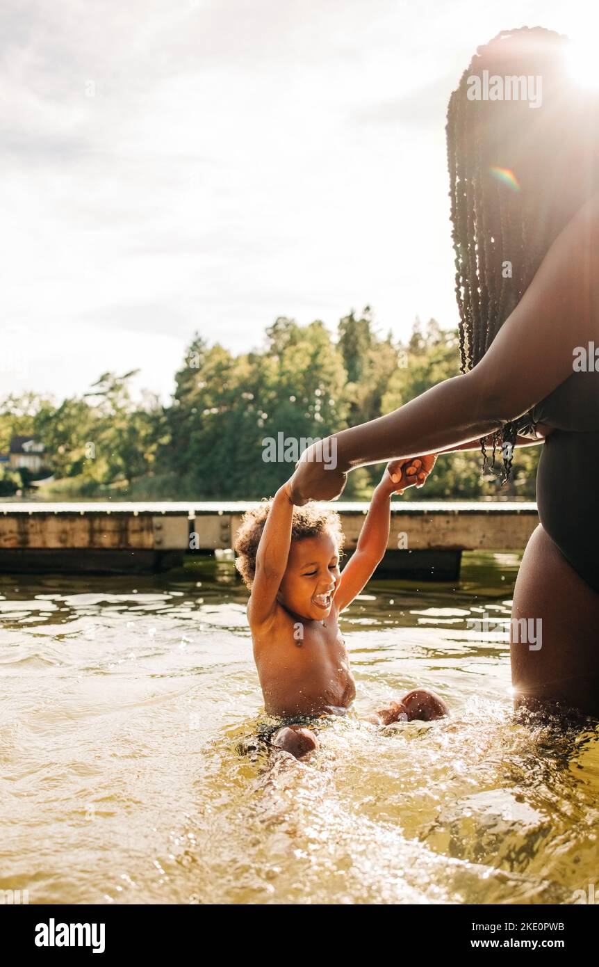 Glücklicher Junge, der im Wasser genießt, während er im Urlaub die Hände der Mutter hält Stockfoto