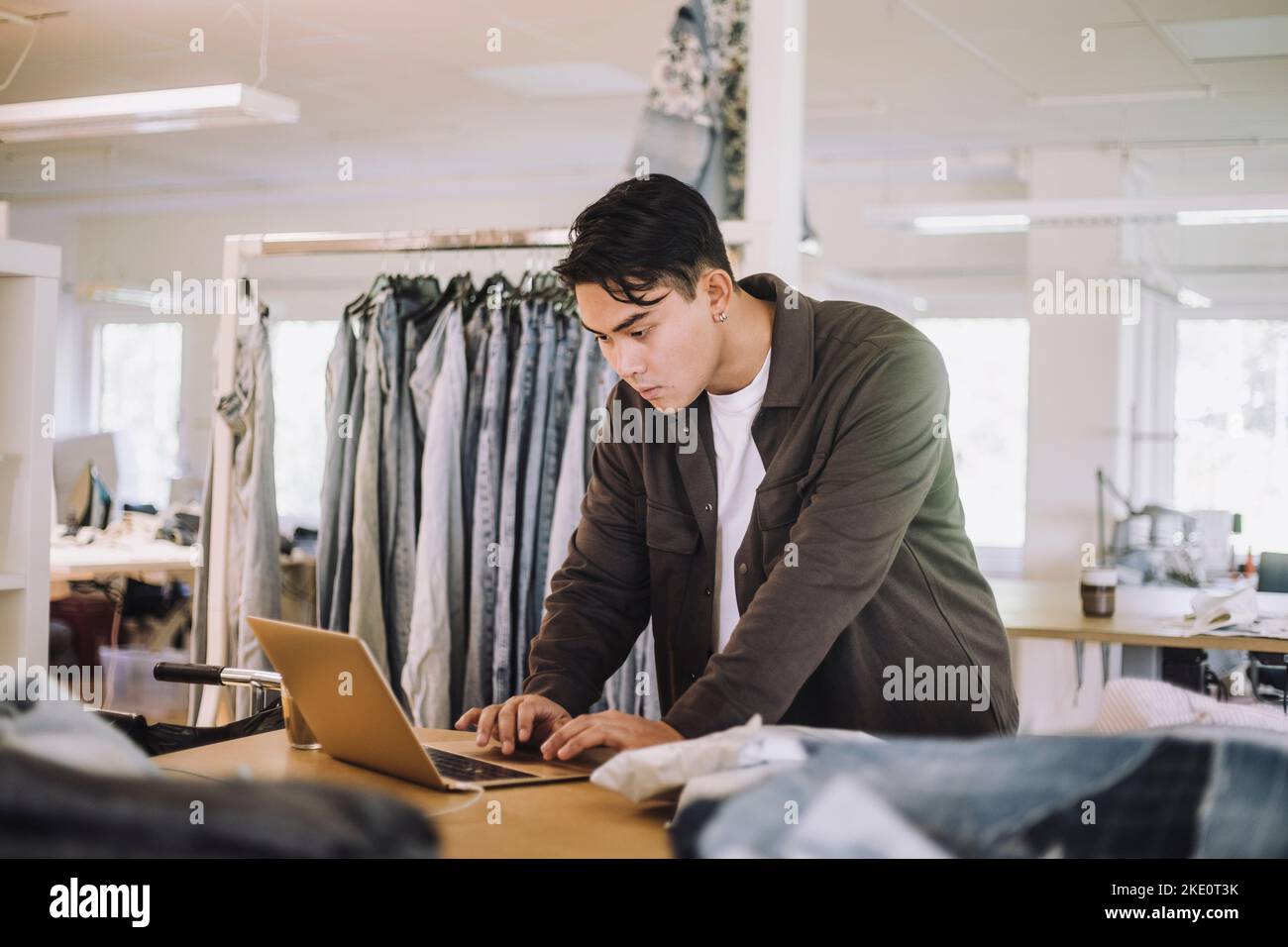 Konzentrierter männlicher Modedesigner mit Laptop in der Werkstatt Stockfoto