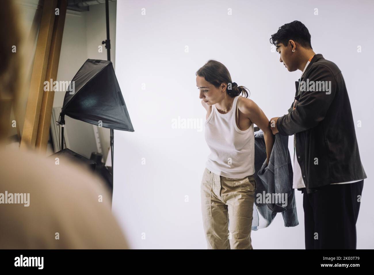Männlicher Designer hilft Modelmodell trägt Jacke während Foto-Shooting im Studio Stockfoto