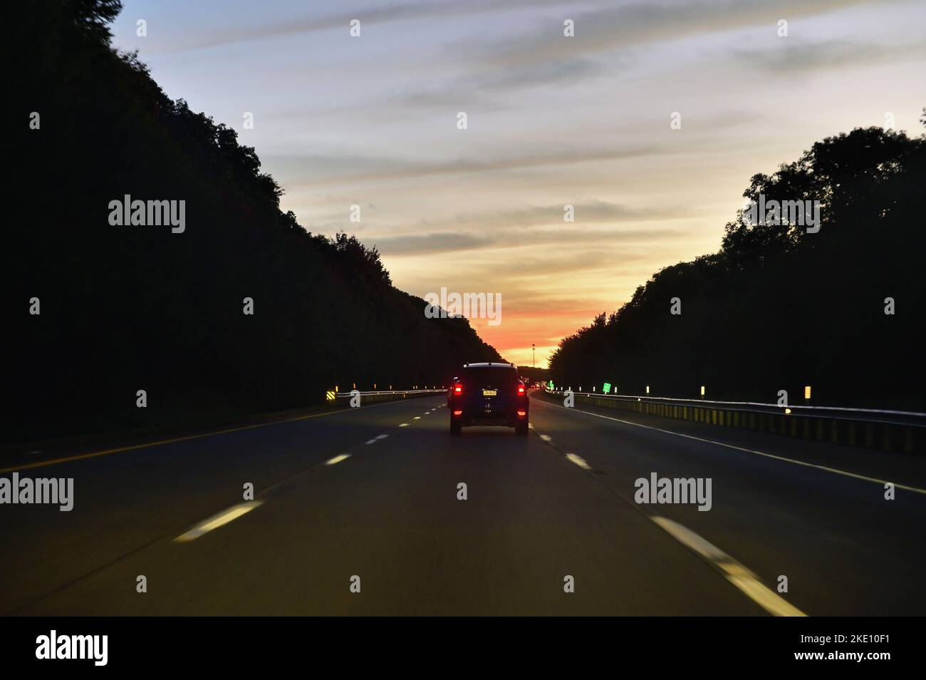 Pennsylvania, USA. Ein einziges Fahrzeug fährt auf einer Autobahn durch eine ländliche Gegend von Pennsylvania in den Sonnenuntergang. Stockfoto