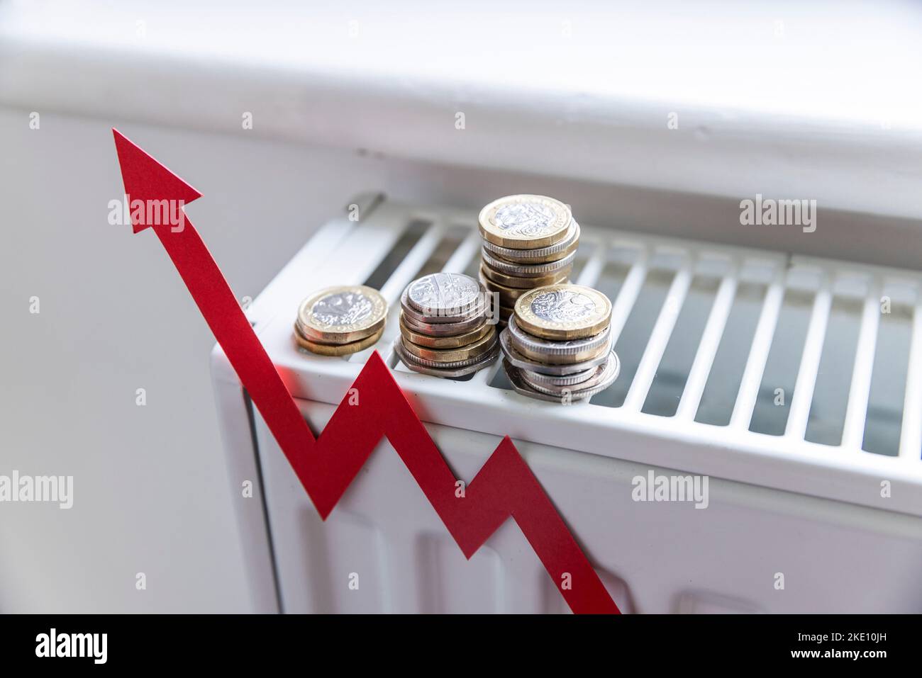 Steigende Energiekosten. Aufsteigender roter Pfeil und Münzen auf einem Heizkörper. Lebenshaltungskosten-Krise Stockfoto