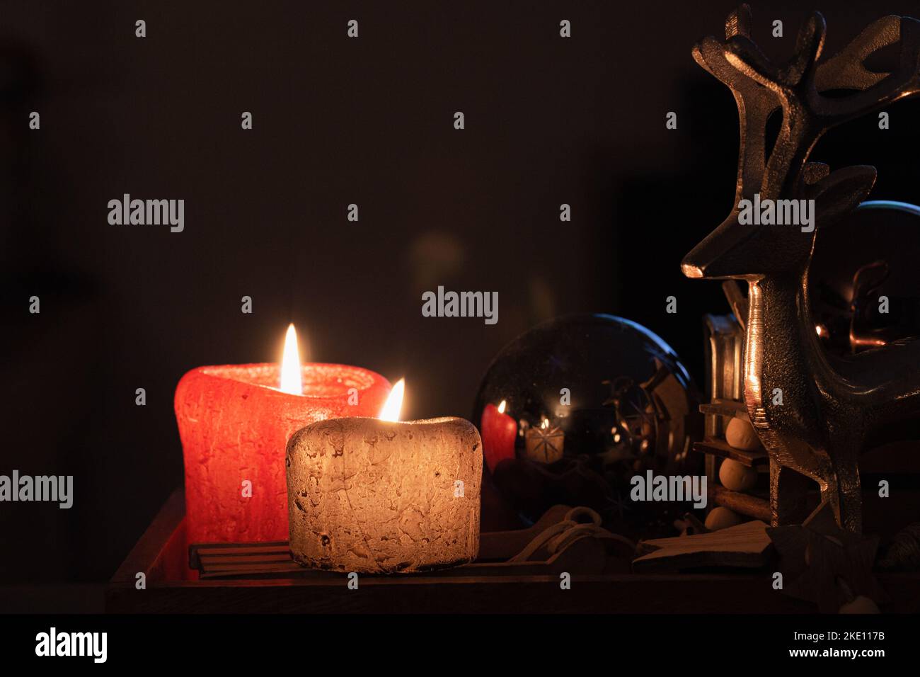 Zwei rote und braune Kerzen, eine weihnachtskugel und ein silberner Hirsch im Kerzenlicht mit Weihnachtsstimmung. Stockfoto