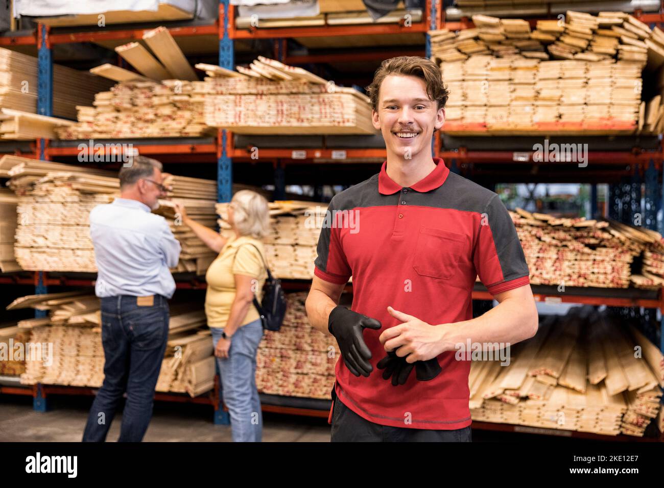 Porträt eines lächelnden Verkäufers, der den Handschuh hält, während er vor dem Regal im Baumarkt steht Stockfoto