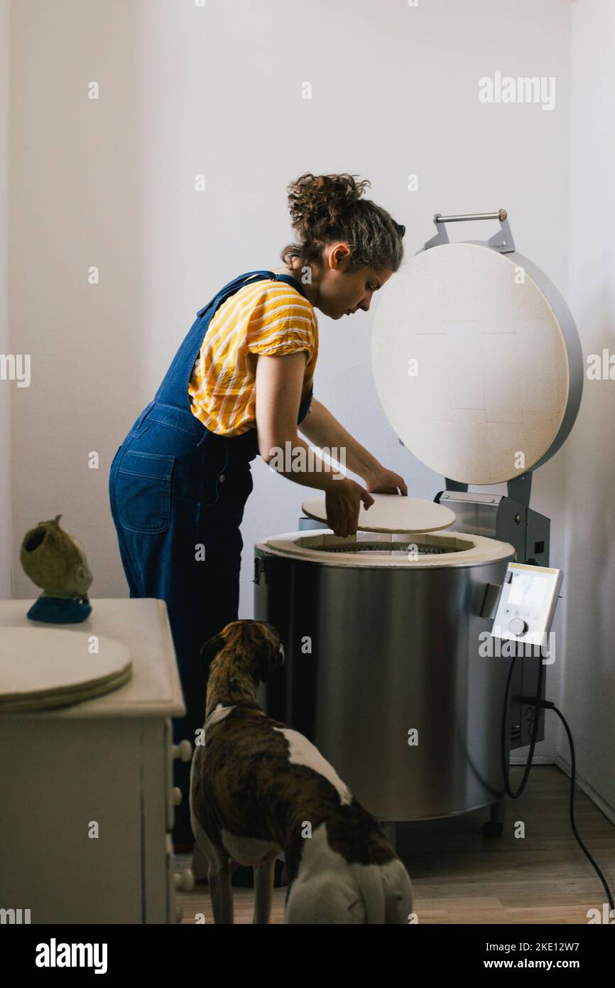 Seitenansicht der weiblichen Handwerker setzen Keramikplatte in elektrischen Ofen während der Arbeit zu Hause Stockfoto