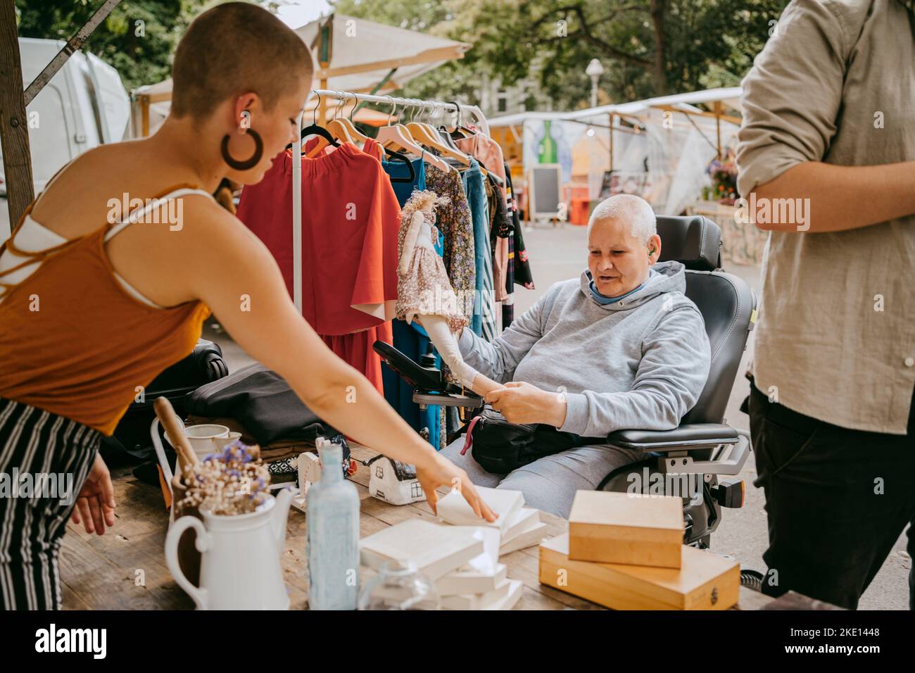 Weibliche Kundin mit Behinderung, die mit dem Besitzer spricht, während sie auf dem Flohmarkt einkaufen Stockfoto