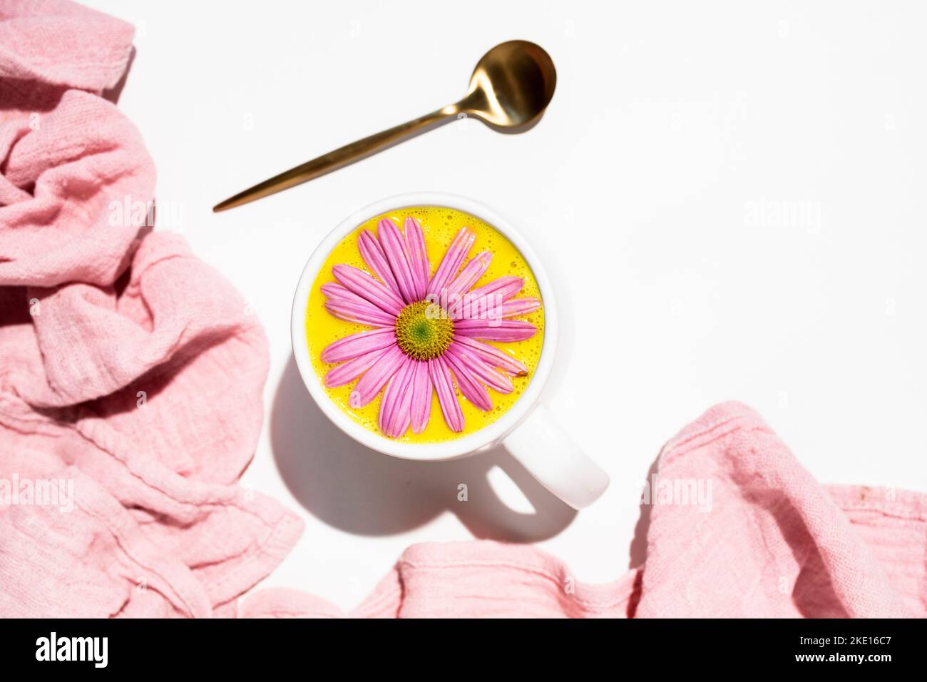 Goldene Milch in einem weißen Becher, verziert mit einer rosa Gänseblümchen Stockfoto