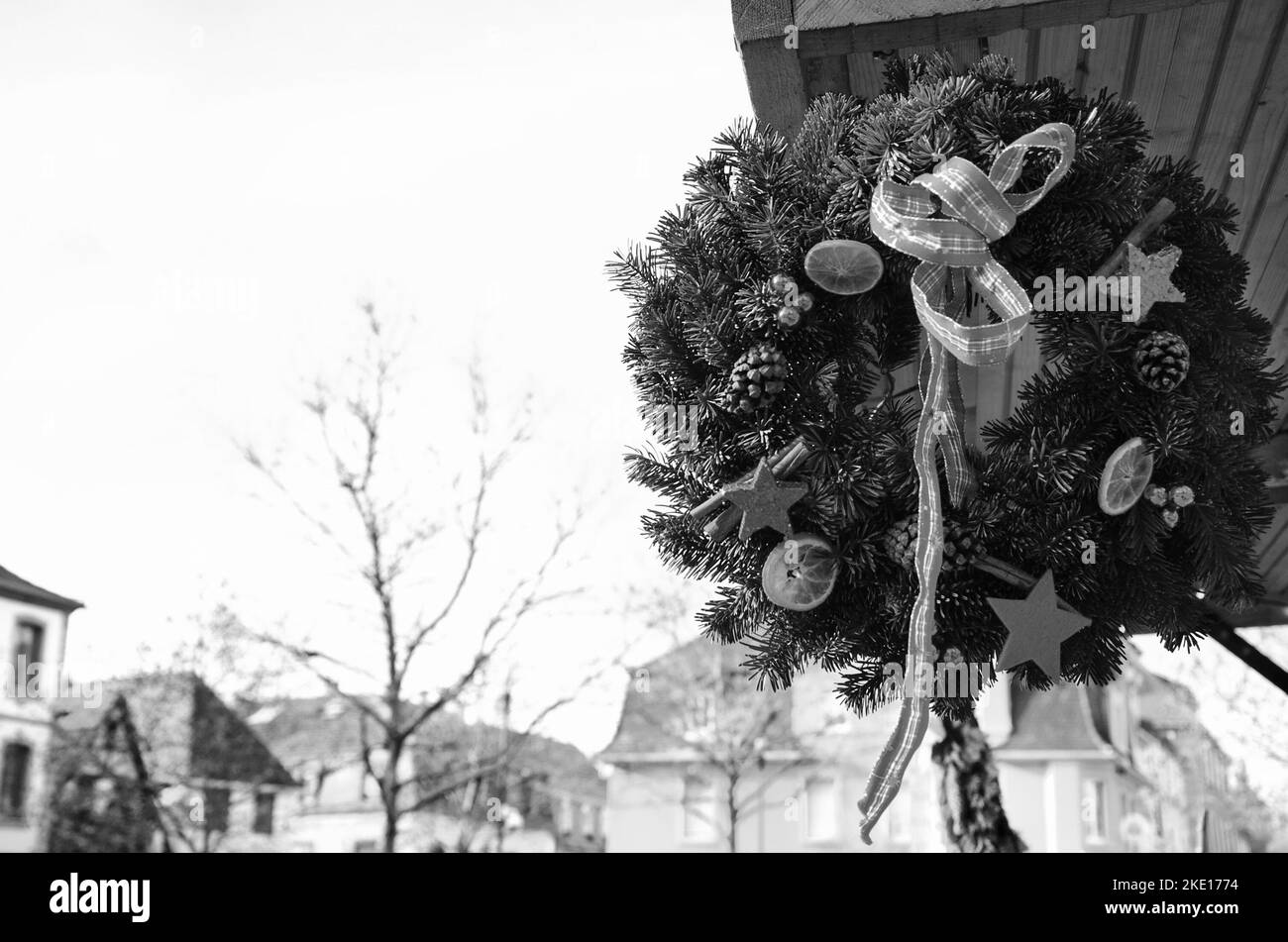 Adventskranz hängt vom Dach des Stalls auf dem Weihnachtsmarkt in Selestat, Frankreich. Selestat ist als Heimat des Weihnachtsbaums bekannt. Schwarzweißfoto Stockfoto