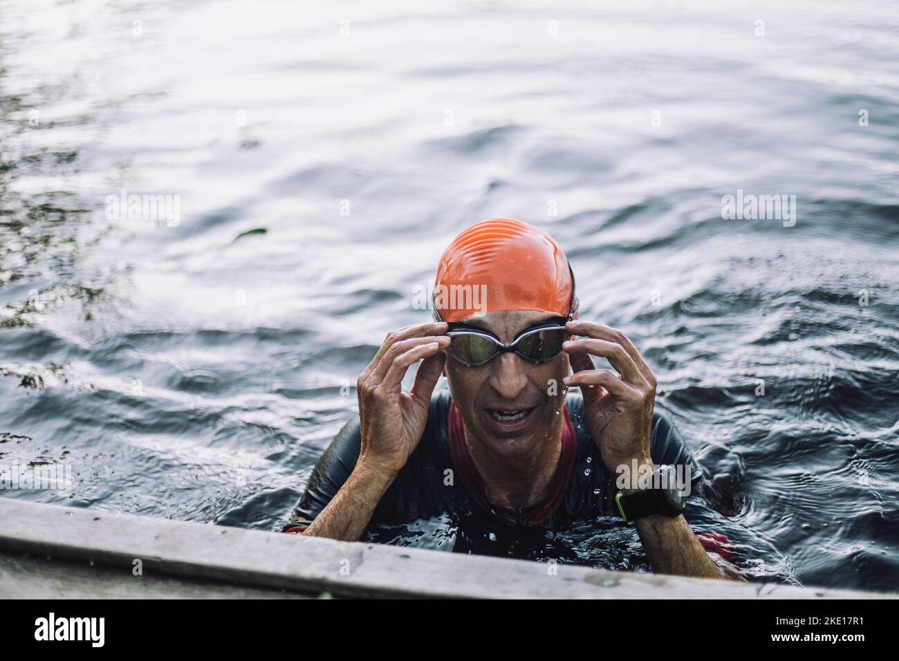 Reifer Mann, der die Brille beim Schwimmen im See justiert Stockfoto