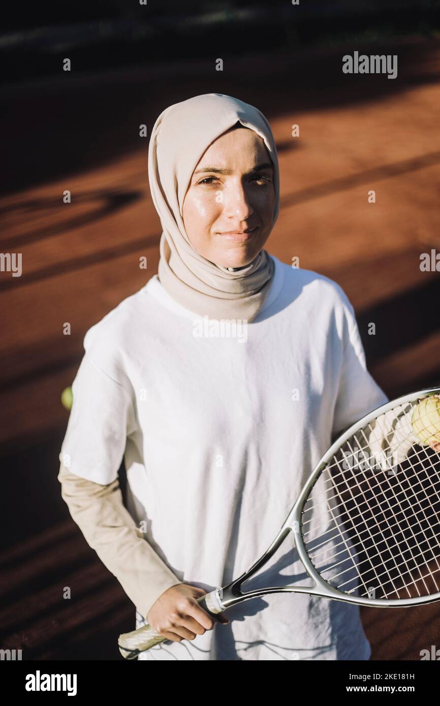 Selbstbewusste Frau mit Kopftuch und Tennisschläger an sonnigen Tagen Stockfoto