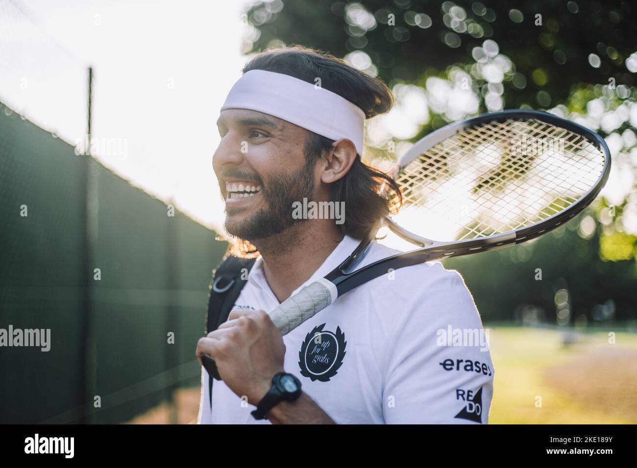 Glücklicher Mann mit Stirnband, der mit einem Tennisschläger davonschaut Stockfoto